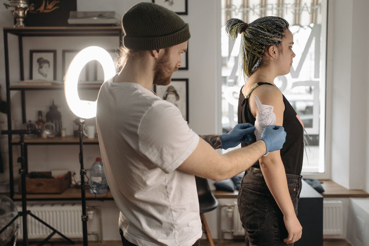 A tattoo artist preparing a stencil on a client’s upper arm