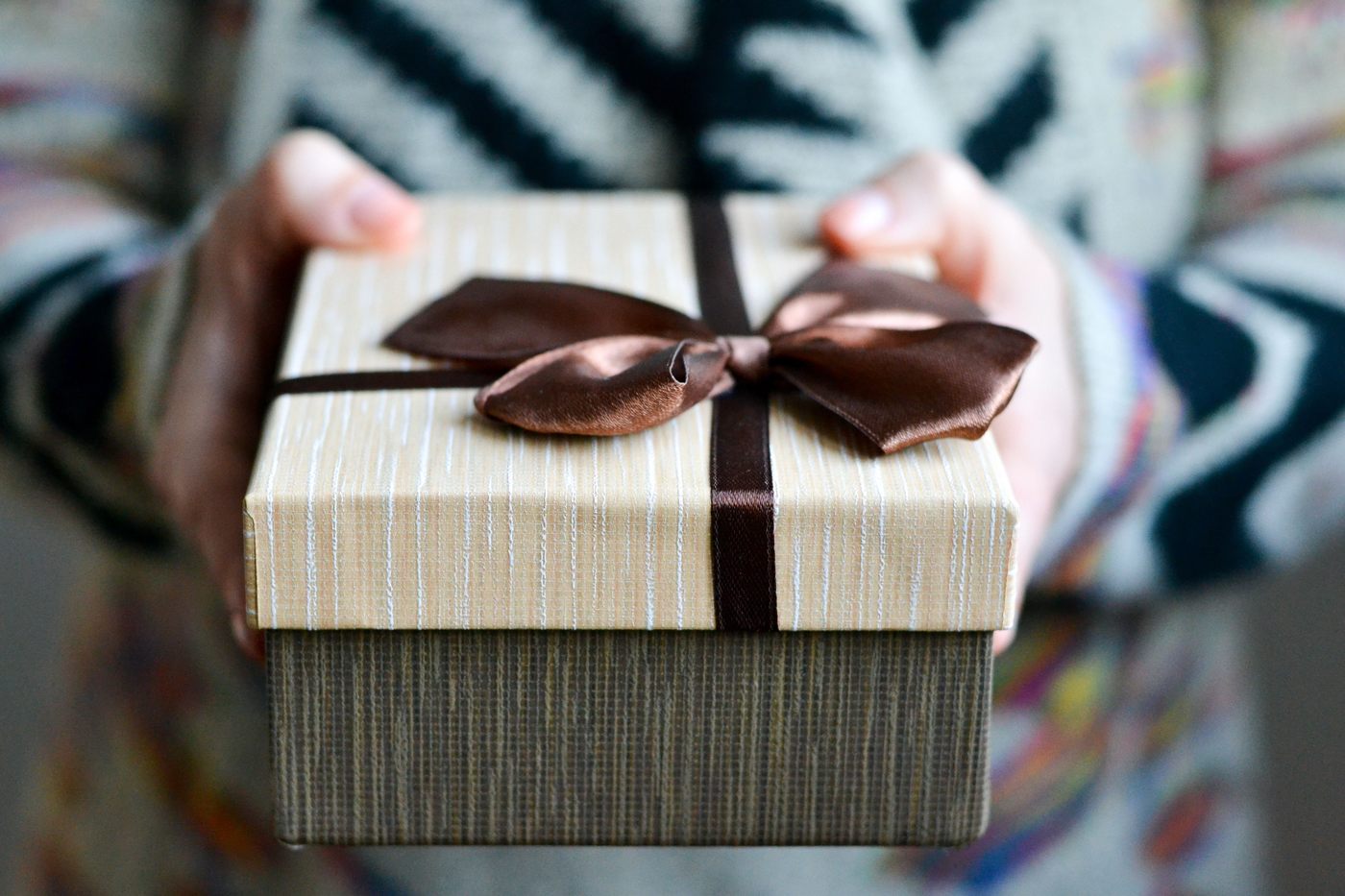 Hands offering a gift box tied with a brown ribbon