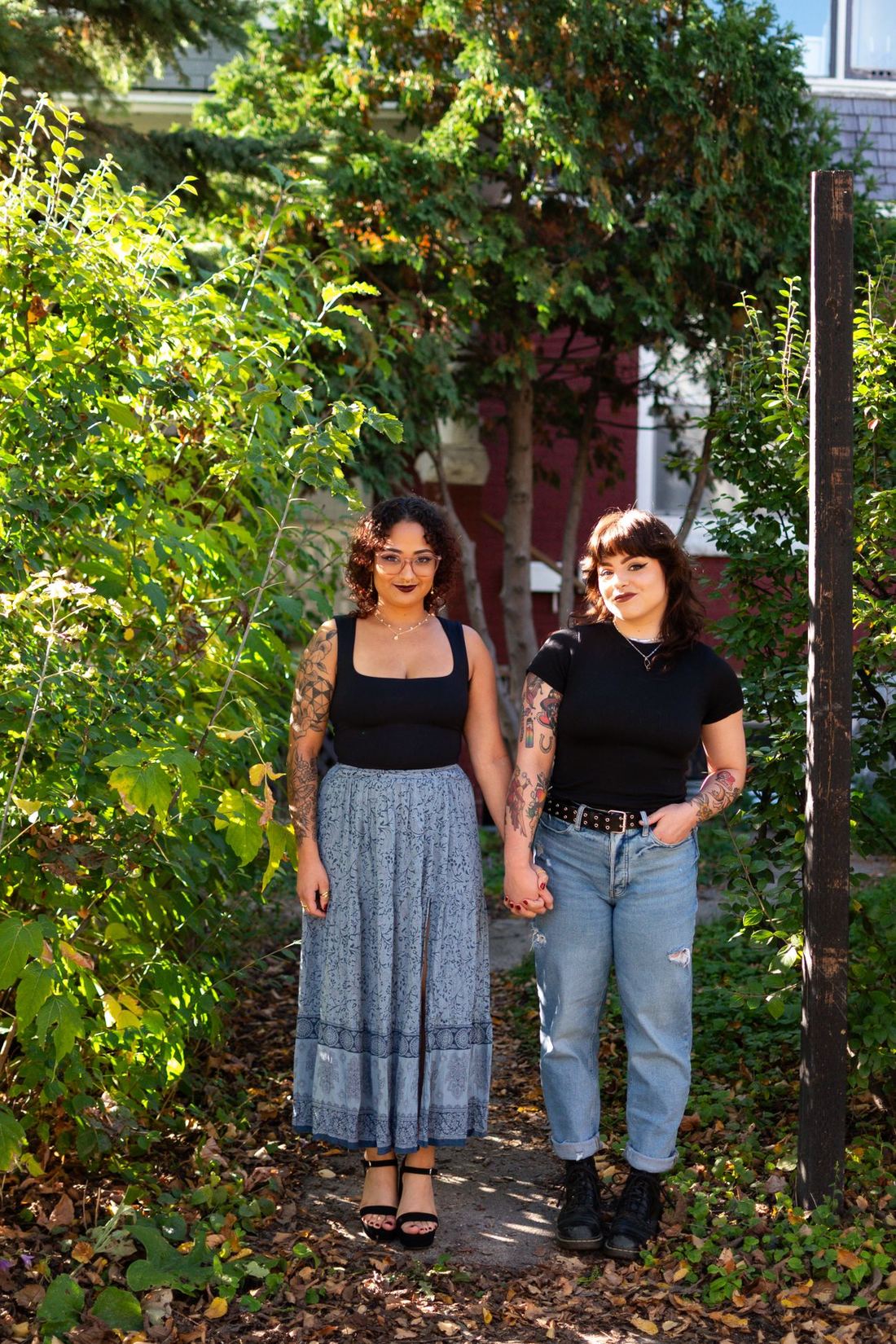 Two tattooed friends holding hands in a sunlit garden